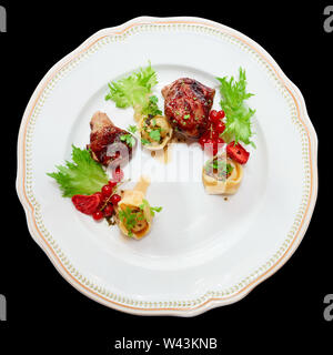 Duck meat with berries and ravioli in plate, isolated on black Stock Photo