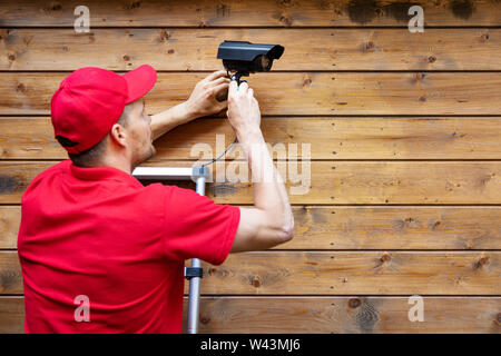 home security - man installing outdoor surveillance camera on wooden wall copy space Stock Photo