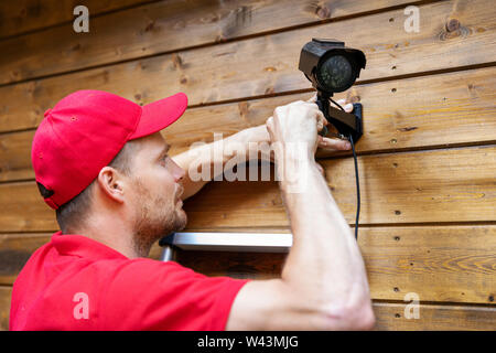 security system technician installing surveillance camera on wooden house wall Stock Photo