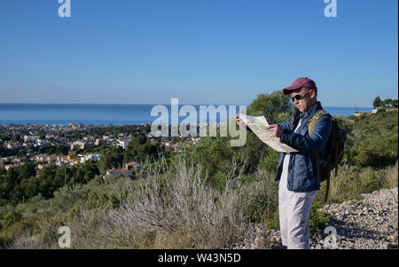 The traveler guy stands on a hillside and looks at a map of the area Stock Photo