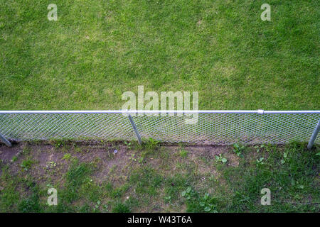 Aerial view of a metal chain link fence with grass on each side. Stock Photo