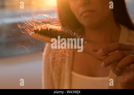 Worried woman holding hairbrush with hair. Stock Photo