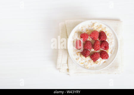 Tasty oatmeal porridge with raspberries in bowl on white table, top view Stock Photo