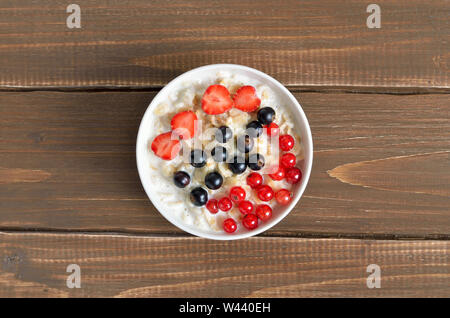 Oatmeal porridge with berries in bowl on wooden table, top view Stock Photo