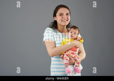 Smiling happy young mother holding baby kid isolated on grey background Stock Photo