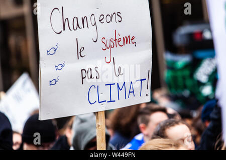 French sign reads change the system not the climate held above crowd of activists during an ecological protest. Urban street filled with environmentalists. Stock Photo