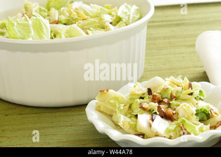 A bowl of coleslaw made from Napa cabbage and sprinkled with toasted sesame seeds and sliced almonds, with an individual serving in the foreground