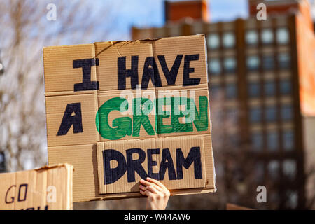 A protestor holds a cardboard sign, reading I have a green dream, viewed close-up as people unite against global warming in a city center.