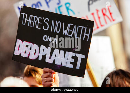 A closeup view of a homemade banner, reading there's no wealth on a dead planet, as a crowd of ecological protestors march on a city street. Stock Photo