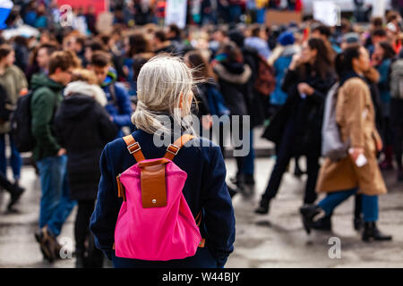 An older woman is viewed from behind, wearing a pink shoulder bag, watching an environmental demonstration on a street in Montreal, Canada Stock Photo