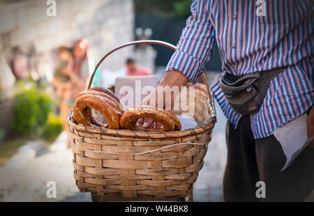 Street vendor selling simit (bread with sesame seeds) in basket and holding one of them to give the customer around Ankara Castle Stock Photo