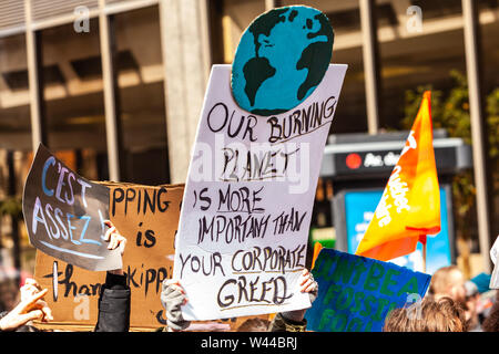 A cardboard sign is viewed close up, saying our burning planet is more important than your corporate greed, as activists march against climate change