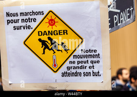 A French poster is viewed close-up, reading we are walking for our survival and depicting a danger sign, held by an eco activist during a street demonstration