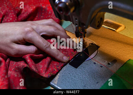 A close up and high angle view of a dressmaker using a heavy duty sewing machine to thread the edge of vintage material. Clothes maker using machinery. Stock Photo