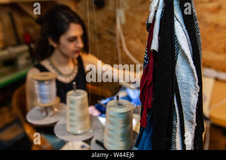 A high angle view of a seamstress hard at work in studio, using an overlock machine with spools of white thread. Creative person in workplace. Stock Photo