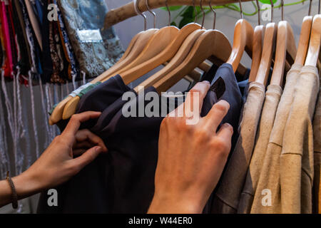 A close-up view on the hands of a young caucasian browsing rails in a small eco-friendly store. Locally handcrafted garments on wooden hangers. Stock Photo