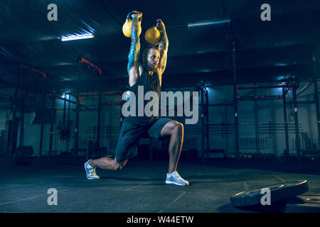Young healthy man athlete doing exercise with the weights in the gym. Single male model training hard and practicing in lunges. Concept of healthy lifestyle, sport, fitness, bodybuilding, cross fit. Stock Photo