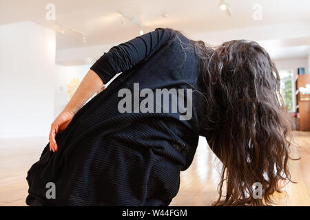 A close up and rear view of a flexible woman, she stretches to the right and her long dark hair touches the wooden floor of a dance studio Stock Photo