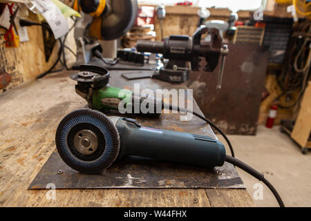 A closeup view of angle grinders with abrasive discs lying on a bench inside a metal workshop. Electrical hand tools used for cutting and grinding metal. Stock Photo