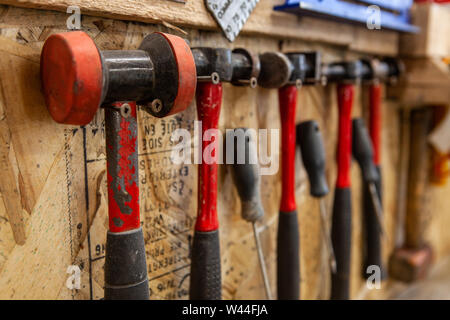 A closeup view on a variety of metalwork hammers and mallets inside a workshop. Various sizes and styles hanging on screws for easy access. Stock Photo