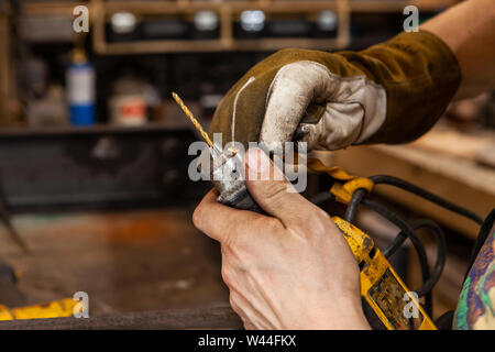 A closeup view on the dirty hands of a metalworker using the chuck of a power drill to replace a spotting bit, used for marking and drilling holes in steel. Stock Photo