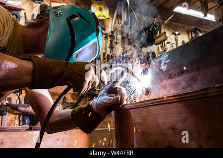 A low angle view of a metalworker operating a spot welder inside his workshop. Welding machine is used to join two pieces of metal. Stock Photo