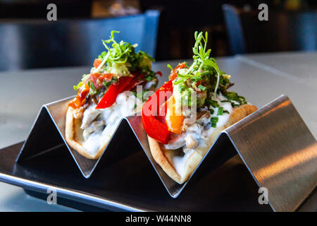 A closeup view of two freshly prepared tacos, filled with colorful salad ingredients, standing in a tray on a table in a modern bistro, healthy snack. Stock Photo