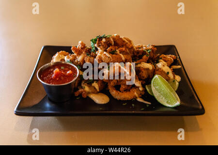 A closeup view of calamari, deep fried squid rings, served with spicy salsa and garnished with lime. Tasty appetizer inside a trendy bistro. Stock Photo