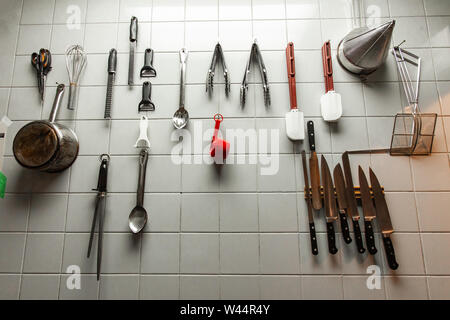 A closeup view of cooking utensils hanging on a tiled wall inside a restaurant kitchen, professional tools are neatly organized for easy access Stock Photo