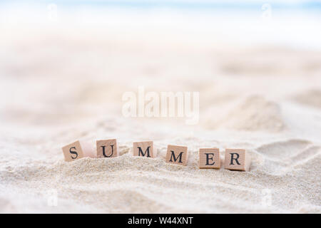 Summer word written on wooden block put on the sand beach. Sea view during daytime with blue sky background. Summer season concept. Stock Photo
