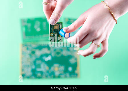 The woman technician is laying a capacitor on the Printed Circuit Board. The concept of computer, service, electronics, hardware, repairing, upgrade a Stock Photo