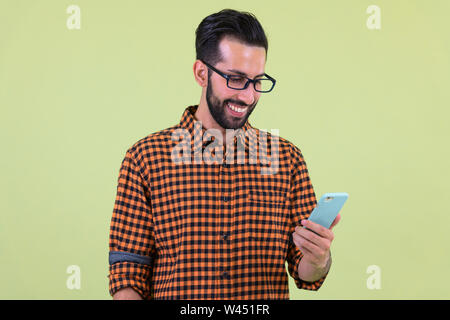 Happy young bearded Persian hipster man using phone Stock Photo