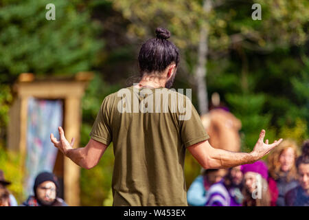 A spiritual guy dressed in bohemian style is seen giving a presentation at a campsite during a festival mixing native cultures and modern traditions Stock Photo