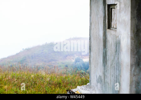 Cracked Exterior cement wall of a old house building and Broken window. Isolated view from beautiful Green forest mountain and Meadow. Stock Photo