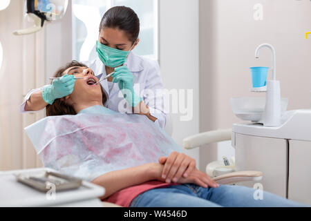 Serious dark-haired female doctor using a dental mirror Stock Photo