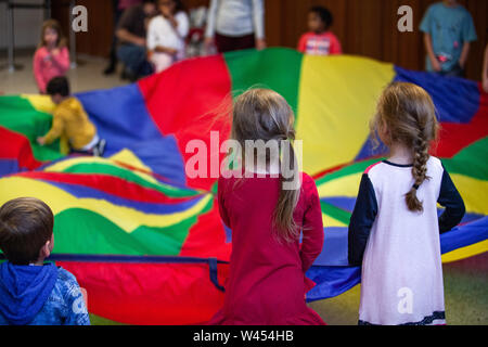 A high angled view of a group of preschool kids, playing cat and mouse with a large rainbow parachute, learning teamwork and cooperation Stock Photo