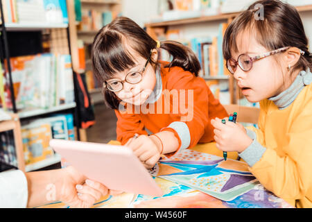 Curious sisters with down syndrome being focused on a tablet Stock Photo