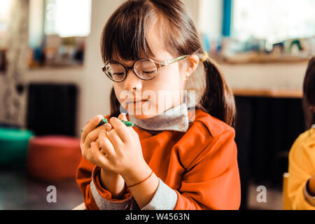 Interested little kid with two ponytails being focused on colorful crayons Stock Photo