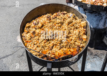 Traditional dish of oriental cuisine - pilaf with meat in a larger vat on the street during the festival Stock Photo