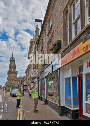 FORRES MORAY SCOTLAND WATERING FLOWERS IN THE HIGH STREET HANGING BASKETS FULL OF FLOWERS Stock Photo