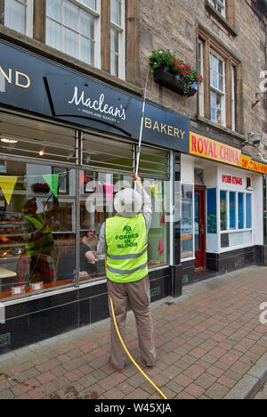 FORRES MORAY SCOTLAND WATERING FLOWERS IN THE HIGH STREET THE HANGING BASKETS FULL OF FLOWERS Stock Photo