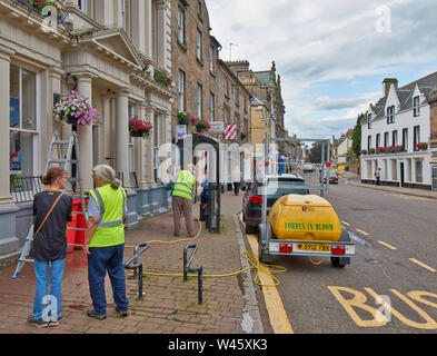 FORRES MORAY SCOTLAND WATERING THE FLOWERS IN HANGING BASKETS ALONG THE HIGH STREET IN SUMMER Stock Photo