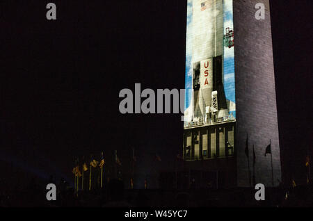 Washington DC, USA. 19th July 2019. American flags guard the base of a life-size, 363ft. Saturn V rocket projected onto the east face of the Washington Monument. The Saturn video projection was commissioned by the National Air and Space Museum in honor of the 50th anniversary of Apollo 11's moon landing. Credit: Tim Thulson/Alamy Live News. Stock Photo