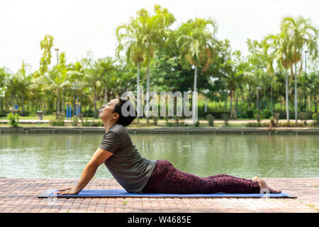 healthy middle aged asian woman doing bhujangasana (cobra pose) yoga pose in city park at the morning. healthy and lifestyle concept. Stock Photo