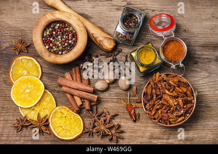 on the table seen from above a wooden mortar with peppercorns, dried orange, anise stars and other types of spicy chili Stock Photo