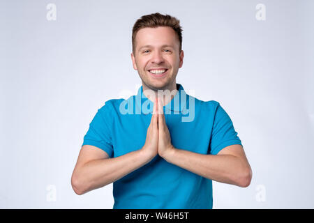 Man in blue shirt holding hands in Namaste welcoming guests Stock Photo