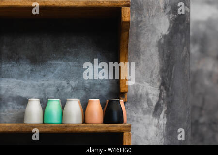 Different colorful coffee cups on wooden shelf in cafe. Background of gray concrete cement wall. Trendy interior design, hipster cafe. Empty space for Stock Photo