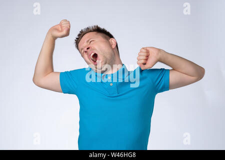 Tired european man in blue shirt feels sleepy, yawns as feels tired, opens mouth widely Stock Photo