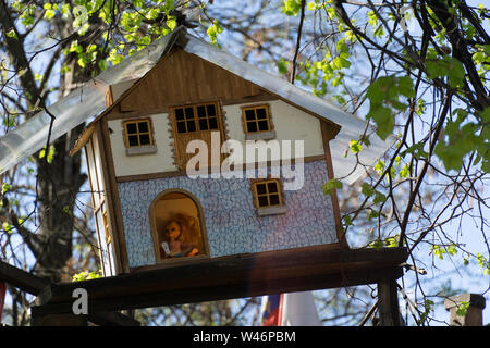 wooden toy house hanging on a tree with baby doll inside on a sunny day Stock Photo
