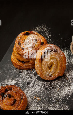 Top view of golden cinnamon rolls with raisins sprinkled with sugar on black background. Stock Photo